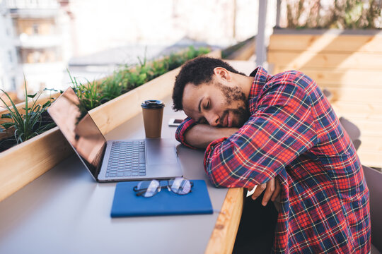 Tired hipster guy fall asleep during deadline remote working on laptop computer, exhausted workaholic with digital netbook technology sleeping at table desktop burnout from overwork lifestyle