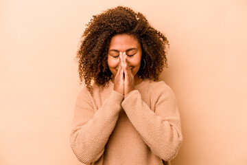 Fototapeta na wymiar Young African American woman isolated on beige background holding hands in pray near mouth, feels confident.