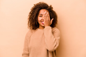 Young African American woman isolated on beige background having fun covering half of face with...