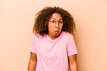 Young African American woman isolated on beige background shrugs shoulders and open eyes confused.
