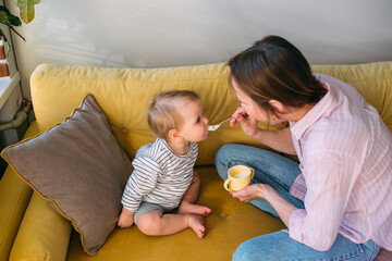 Mom feeds a small child at home with yogurt from a spoon. Family concept