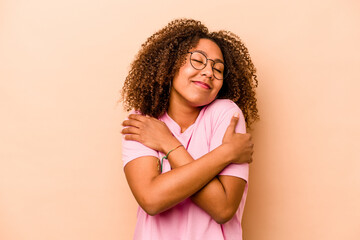 Young African American woman isolated on beige background hugs, smiling carefree and happy.