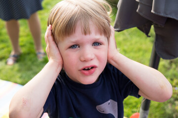 a toddler is closing his ears because it's too loud. High quality photo