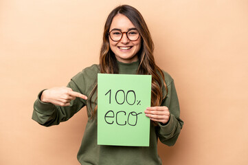 Young caucasian woman holding 100% eco placard isolated on beige background person pointing by hand to a shirt copy space, proud and confident