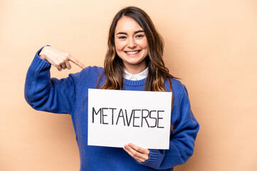 Fototapeta na wymiar Young caucasian woman holding a metaverse placard isolated on beige background person pointing by hand to a shirt copy space, proud and confident