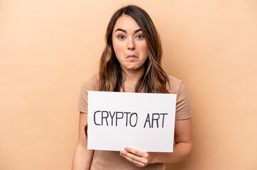 Young caucasian woman holding a crypto art placard isolated on beige background shrugs shoulders and open eyes confused.