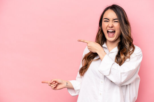 Young caucasian woman isolated on pink background pointing with forefingers to a copy space, expressing excitement and desire.