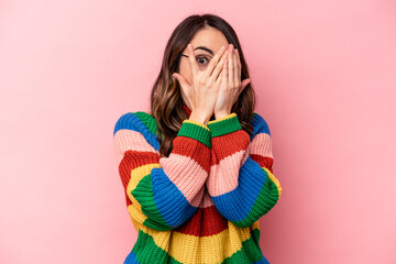 Young caucasian woman isolated on pink background blink through fingers frightened and nervous.