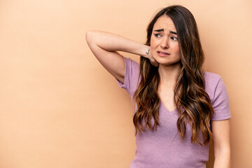 Young caucasian woman isolated on beige background touching back of head, thinking and making a choice.