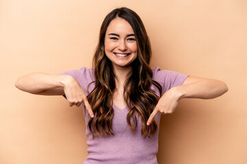 Young caucasian woman isolated on beige background points down with fingers, positive feeling.