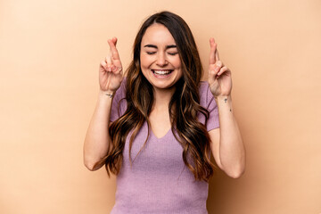 Young caucasian woman isolated on beige background crossing fingers for having luck