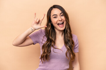 Fototapeta premium Young caucasian woman isolated on beige background showing a horns gesture as a revolution concept.