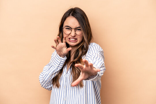 Young caucasian woman isolated on beige background showing claws imitating a cat, aggressive gesture.
