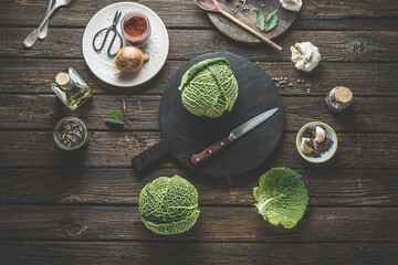Food background with two whole raw savoy cabbage on rustic wooden kitchen table with cutting board,...