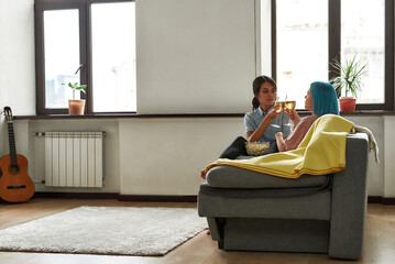 Two happy lesbian girls toasting with champagne on sofa