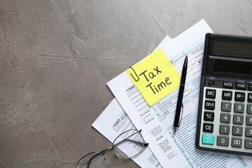 Reminder note with words TAX TIME, documents, glasses and calculator on grey table, flat lay. Space...