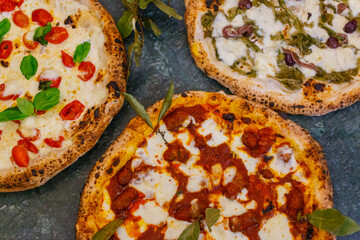 Tris di pizze napoletane condite con sugo di pomodoro, mozzarella di bufala, salsiccia, pomodori, scarole, olive e acciughe