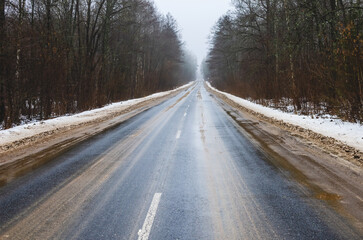 Asphalt road going into the distance during the thaw in winter. Dirty roadside from reagents