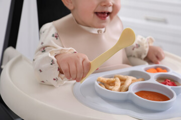 Obraz na płótnie Canvas Little baby eating food in high chair indoors, closeup