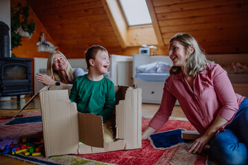 Boy with Down syndrome with his mother and grandmother playing with box together at home.