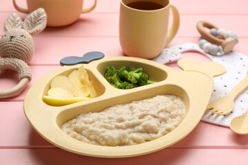 Plastic dishware with healthy baby food on pink wooden table, closeup