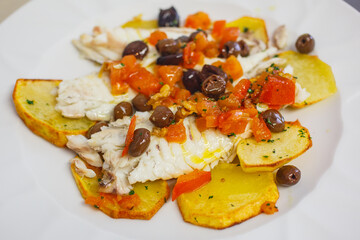 Piatto con pesce cotto al forno con olive nere, pomodori e patate al forno servito in un ristorante elegante