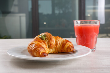 Cornetto caldo ripieno di crema al pistacchio e decorato con zucchero a velo servito a colazione in un bar con un succo di frutta all'arancia rossa