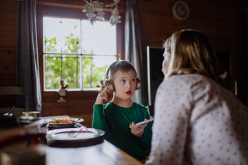 Boy with Down syndrome with his mother having lunch and using smartphone at home
