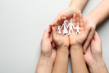 Parents and child holding paper cutout of family on light background, top view. Space for text