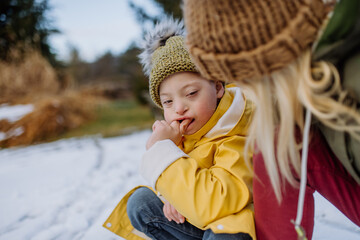 Boy with Down syndrome with his mother playing with snow in garden.