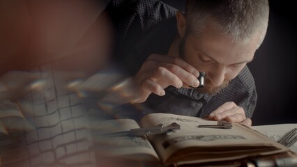 A close-up of the hands of a male jeweler measuring the size of the future product. A book on...