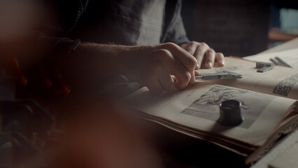 A close-up of the hands of a male jeweler measuring the size of the future product. A book on creating jewelry