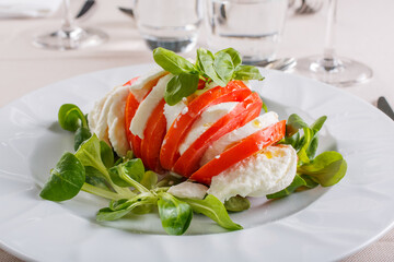Caprese mediterranea composta a strati con mozzarella di bufala, pomodoro fresco e basilico fresco servita in un ristorante elegante