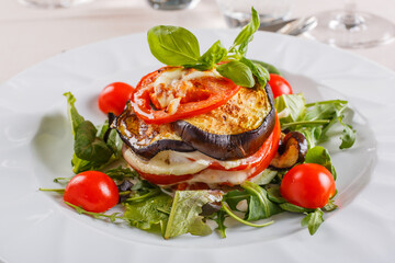 Millefoglie di melanzane fatta con melanzane grigliate, mozzarella filante, pomodori e basilico fresco servita in un ristorante elegante
