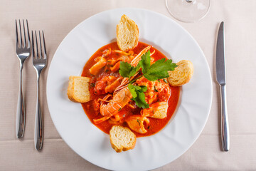 Zuppa di pesce con crostini di pane e prezzemolo servita in un ristorante elegante con un calice di vino bianco