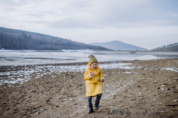 Happy little boy with Down running outside by lake in winter.