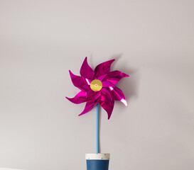 Bright cyclamen colored windmill toy growing out of a blue and white flower pot on minimal...