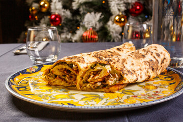 Tronchetto fatto con pasta per la pizza cotto al forno e ripieno di salsiccia, friarielli e provola affumicata fotografato su un tavolo da ristorante davanti ad un albero di natale