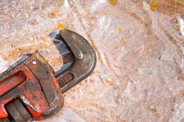 A dirty adjustable pipe wrench is placed on ground at construction working area. Industrial...