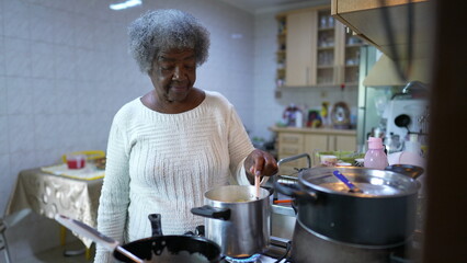 A black older woman cooking at kitchen stirring pot