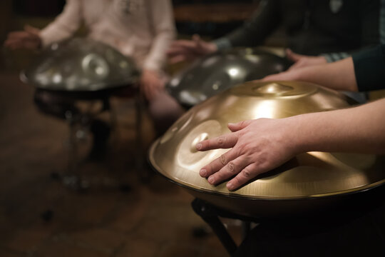 A musician's hand playing the handpan with other people. Handpan is a term for a group of musical instruments that are classified as a subset of the steelpan. 