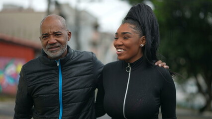 A black father and teen daughter walking together outside in street