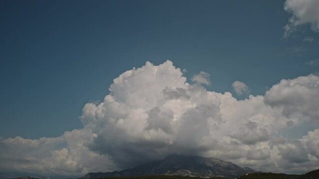 White dramatic clouds, cumulus, forming over the mountain peak with blue sky in the background. Time lapse. Montenegro.
