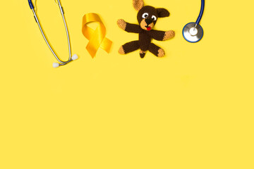 Concienciación sobre el cáncer infantil Cinta lazo amarilla con oso de juguete y estetoscopio sobre un fondo amarillo liso y aislado. Vista superior. Copy space - obrazy, fototapety, plakaty