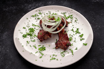 Grilled pork ribs with onions and herbs, on a dark background