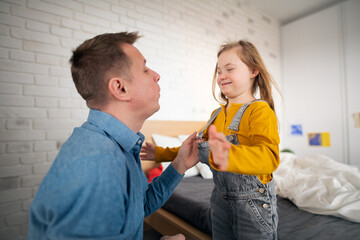 Father helping his little daughter with Down syndrome to wear trousers at home.