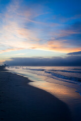 Fototapeta na wymiar Blue sky and orange clouds reflect in the receding waves at the beach