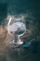 blades from a razor lie in a glass, smoke around the glass