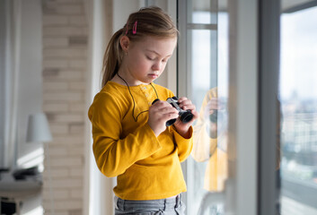 Curious little girl with Down syndrome with binoculars looking through on window at home.