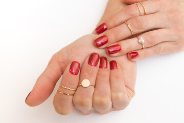 Manicure gel polish of red color with sparkles on female hands with rings